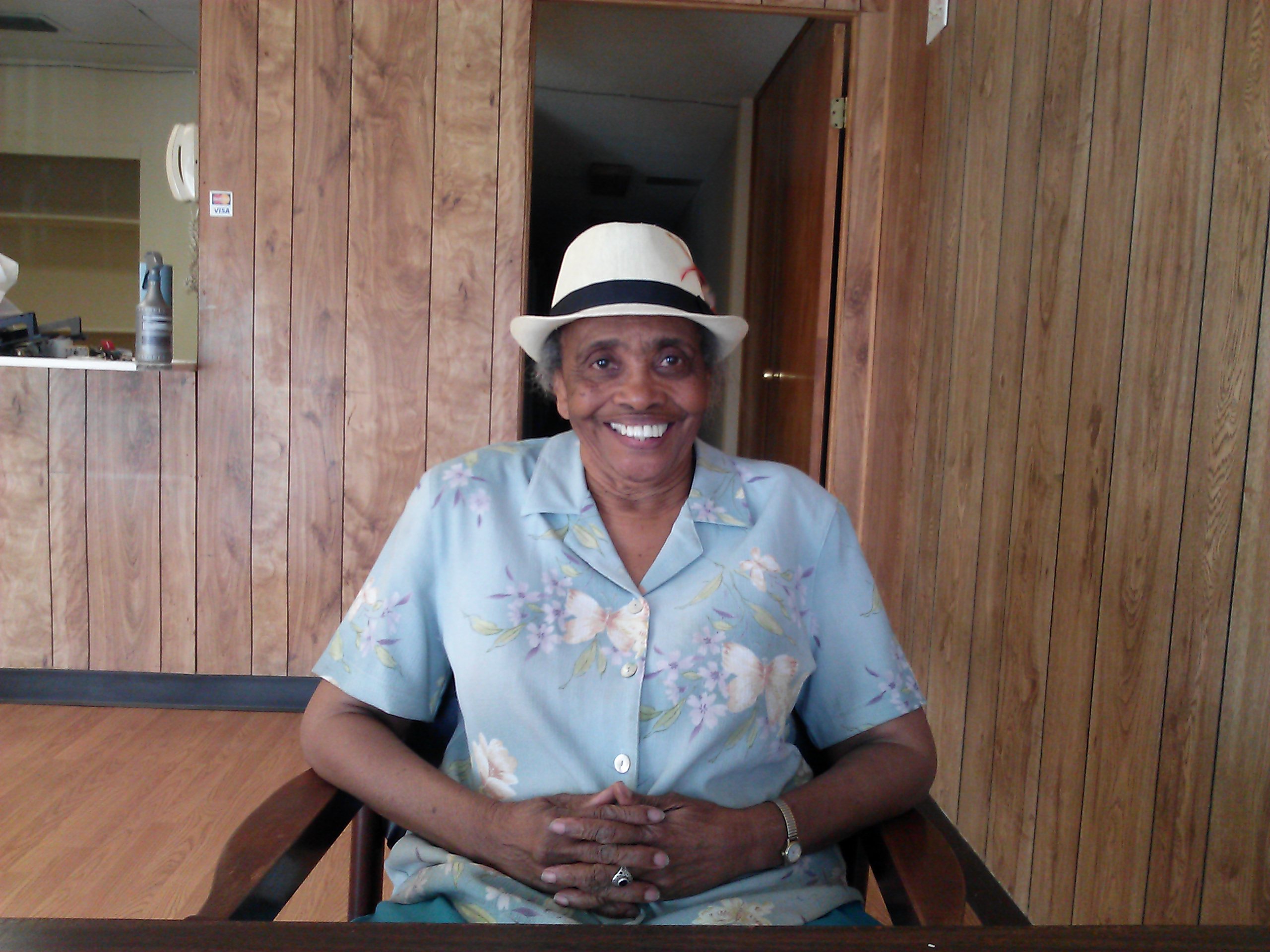 Evelyn sits smiling in chair in a wood paneled room