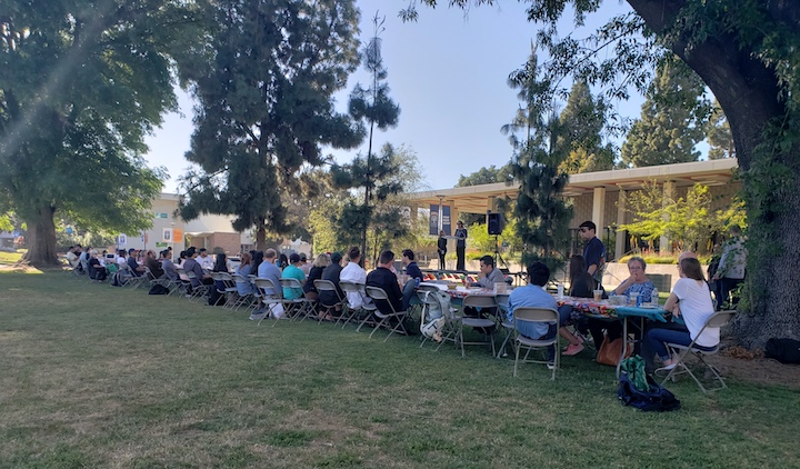 Students and community members sit together at long table on CSUF campus lawn