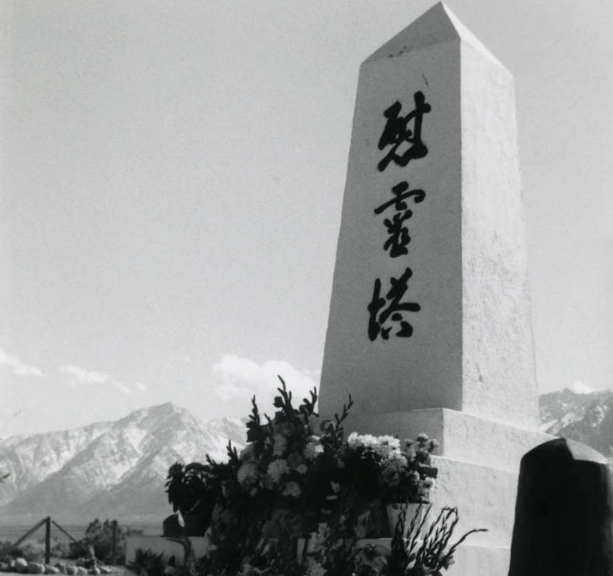 Black and white side view of Manzanar Memorial Tower with flowers at base