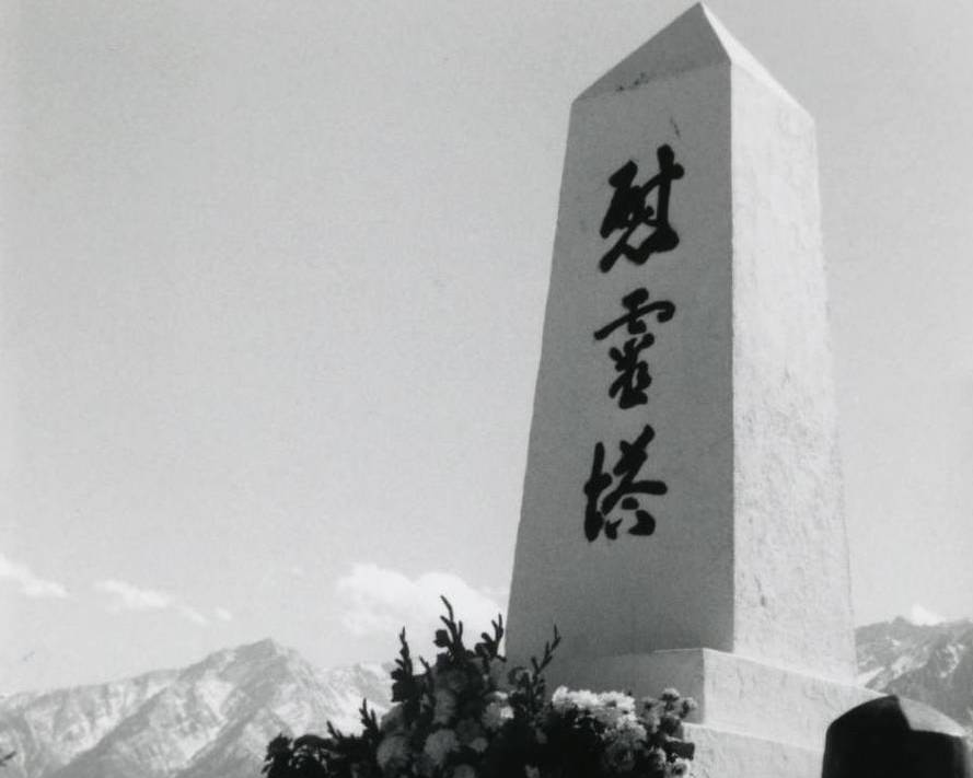 Black and white side view of Manzanar Memorial Tower with flowers at base