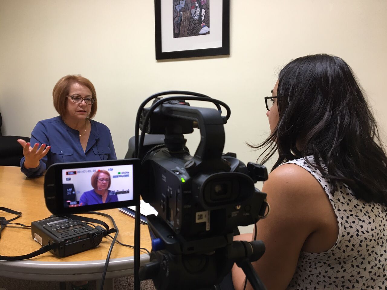Analia Cabral interviews Maria Elena Durazo. Seated at table with video camera in foreground.